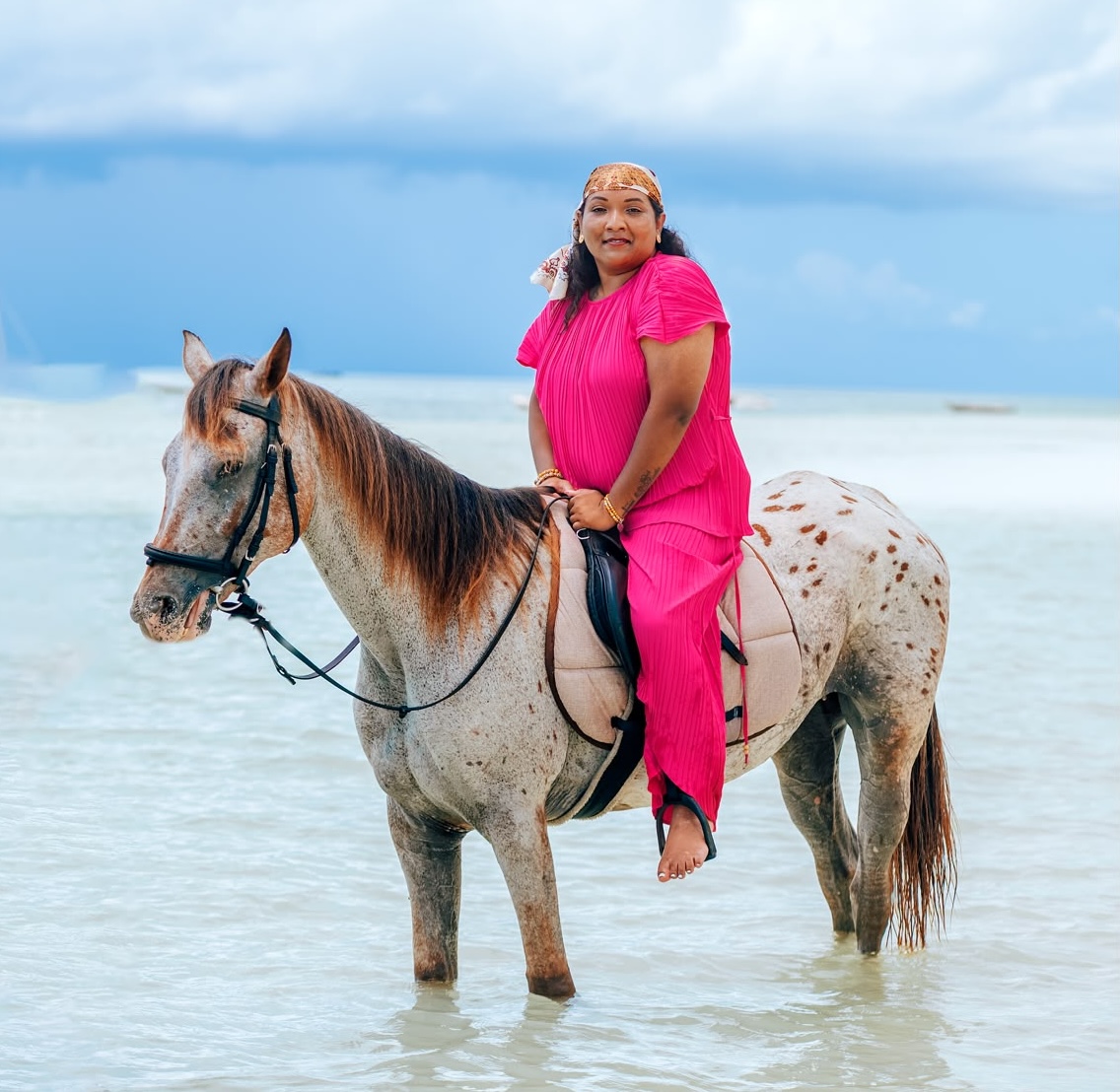 Beach horse riding in Paje, Zanzibar — guest in a bright pink outfit riding a spotted horse through shallow turquoise water