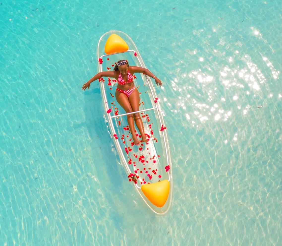Transparent kayak and drone photoshoot in Paje, Zanzibar — couple relaxing on a clear kayak surrounded by flower petals on turquoise water